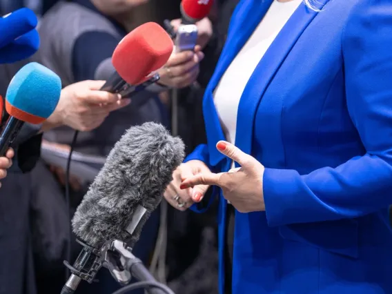 Woman in a blue suit and red nail polish stands in front of microphones