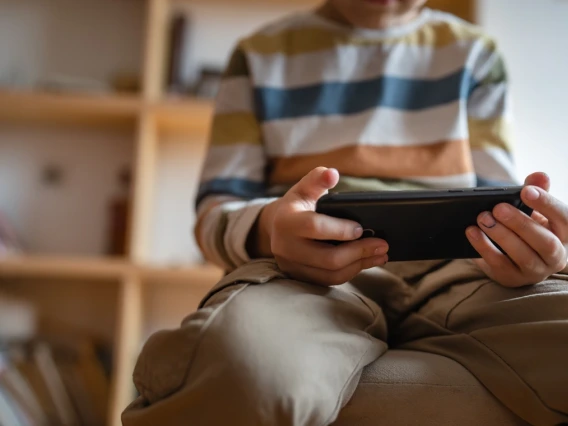 A young child sits, wearing a striped shirt and holds a phone