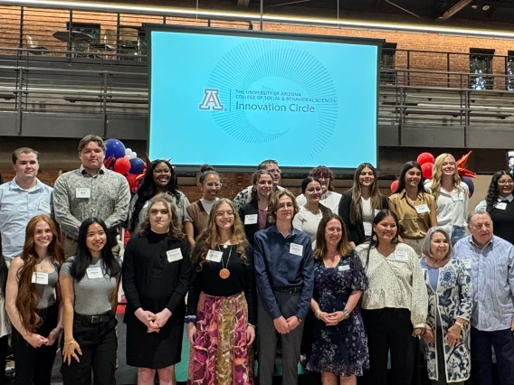 Large group of students, faculty and donors stand in a group in a gym, smiling for a photo