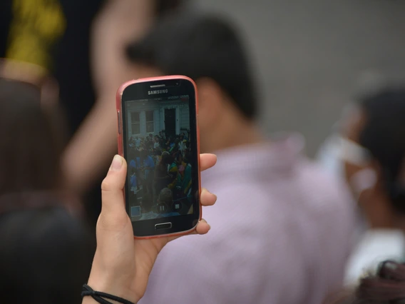Hand holding a cell phone that is taking video of a crowd of people