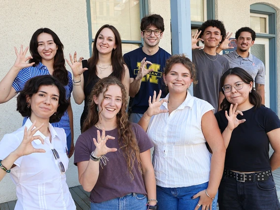 Nine students stand outside and show the sign for "Wildcats"