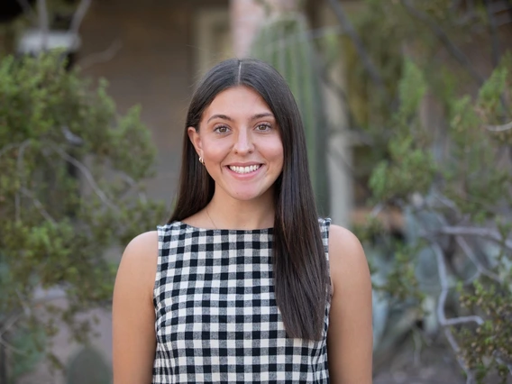 Grace is in front some green trees and cacti wearing a black and white striped top with her hair down. 