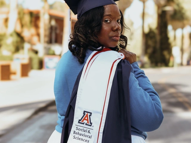 A graduating student stands outdoors wearing a navy cap decorated with flowers and a white graduation stole with the University of Arizona logo and “Social & Behavioral Sciences” printed on it. She looks back over her shoulder toward the camera, with trees and campus buildings blurred in the background.