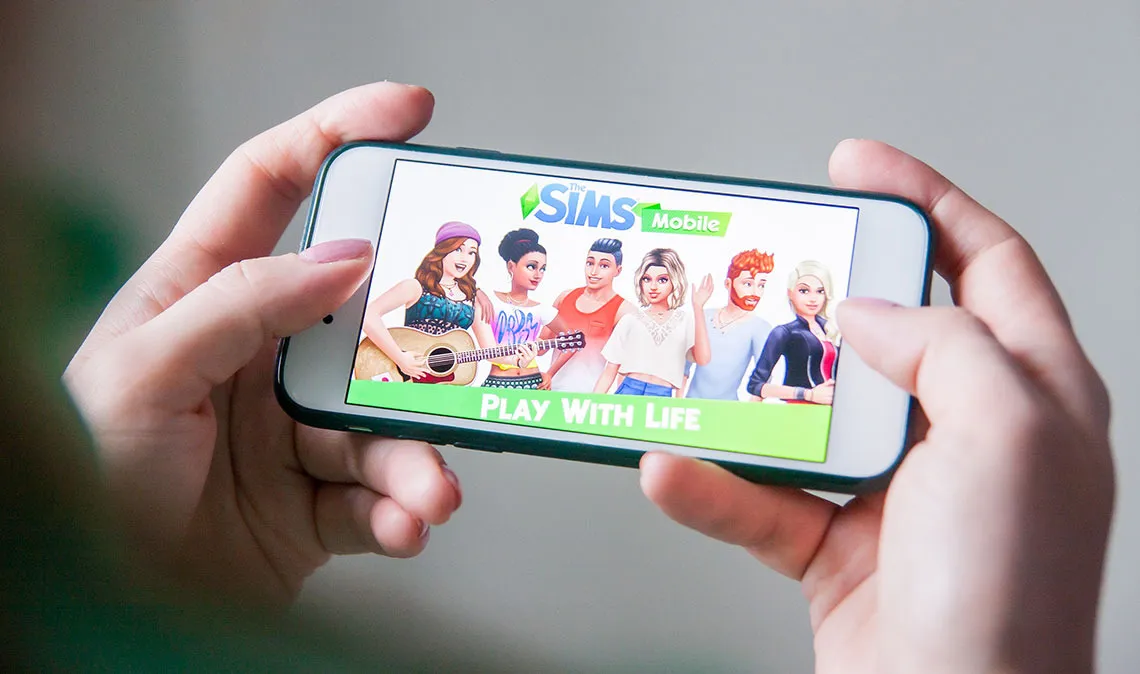 Human hands holding a phone with The Sims on the screen
