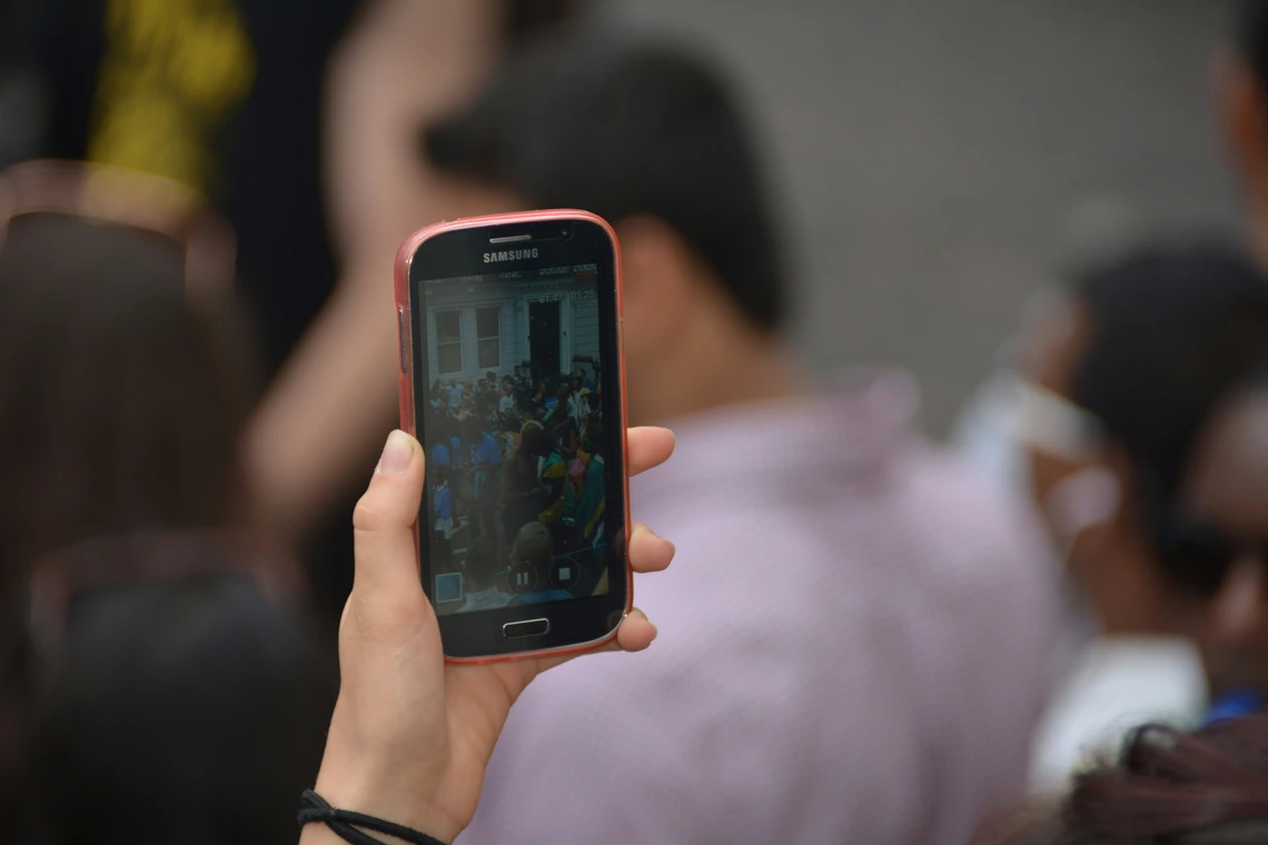 Hand holding a cell phone that is taking video of a crowd of people