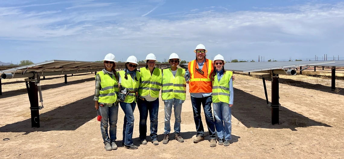 Greg Barron-Gafford and four members of his team, wearing safety vests and hard hats stand outside next to solar panels