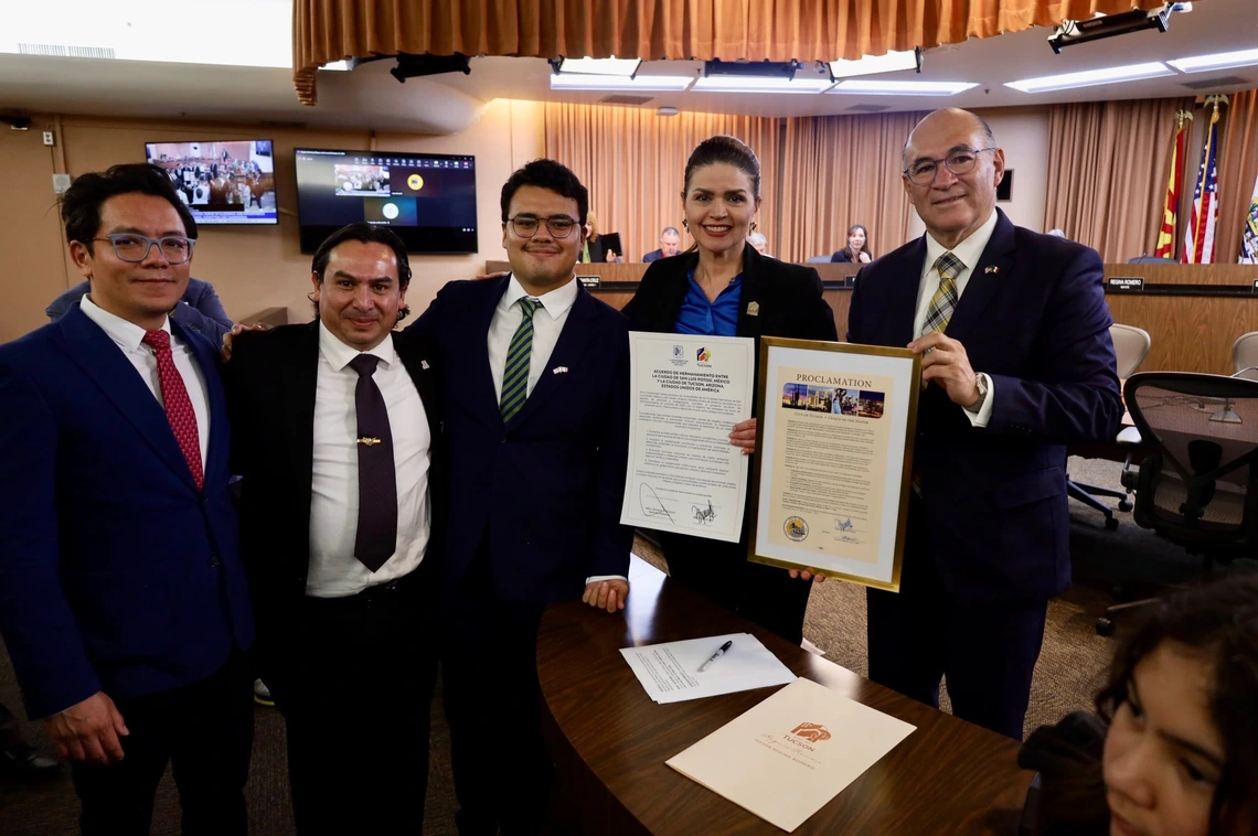 Four men and one woman in black suits stand together, holding ceremonial proclamations