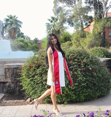Young woman stands outside in white dress and graduation regalia