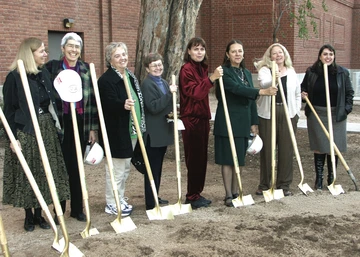Eight women stand outside in front of golden shovels for a groundbreaking ceremony