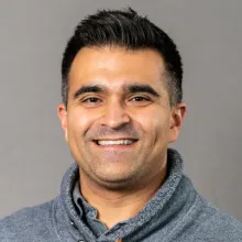 A man with black hair and a gray sweater