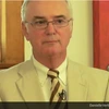 George Cunningham, in a cream colored suit and wearing glasses, stands in front of a brightly colored piece of art