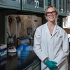 Student stands in a white lab coat and safety glasses in a lab