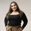 Woman with long brown hair and wearing a black top and brown pants