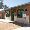 Two renovated brick homes with green trim. There is a sign on an easel and chair and benches set up for guests.