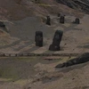 Moai statues partially buried in the slopes of Rano Raraku quarry on Easter Island, with several stone heads standing upright and others tilted or lying on the ground across a barren, rocky hillside