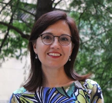 Woman with brown hair and glasses stands outside in the trees