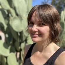 woman with short brown hair and wearing a tank top stands outside