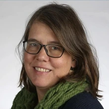 Woman with brown hair and wearing glasses and a green scarf