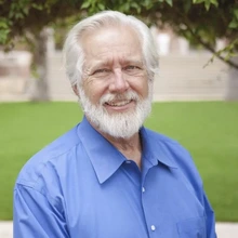 Man with white hair and beard in a blue shirt standing outside