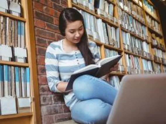 Girl sitting in library with book.