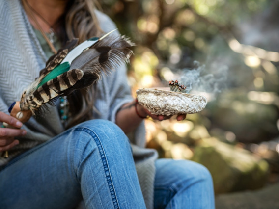 woman in jeans engaging in smudging, a rite that involves burning of sacred herbs