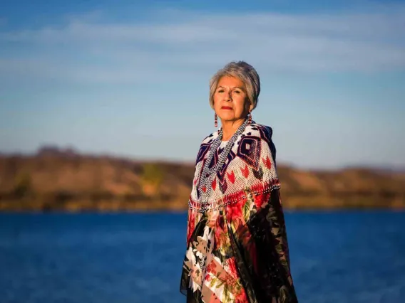 Amelia Flores stands in front of a body of water, wearing Indigenous clothing