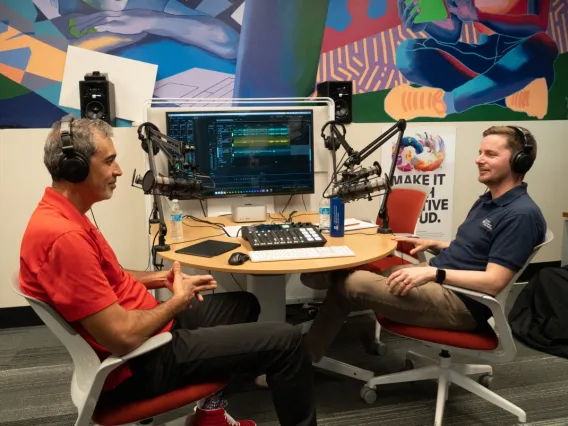 Two men sit in a recording studio with a colorful background