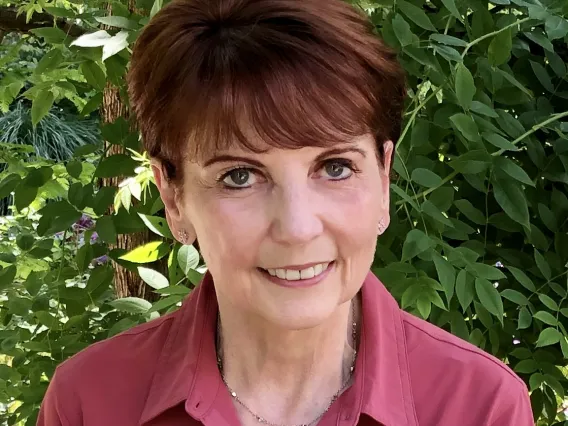 A woman with short brown hair and red shirt sits outside, smiling