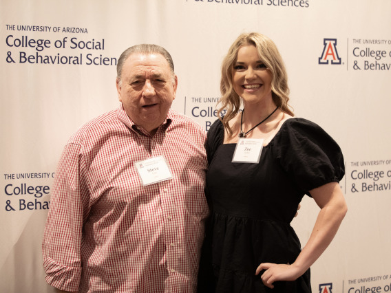 A man in a red shirt standing with a blonde woman in a dark blue dress