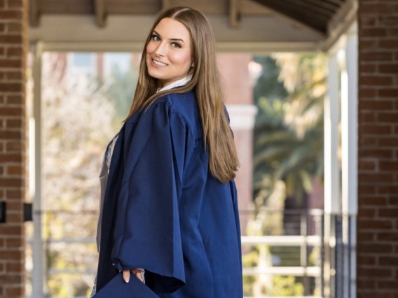 Woman with long hair standing outside in a blue graduation gown