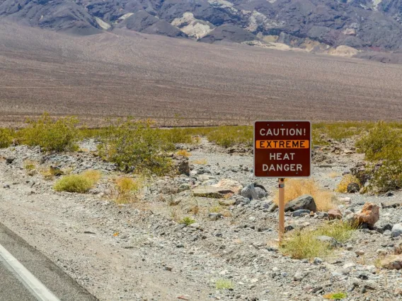 Long stretch of highway in a desert setting with a sign that warns of heat