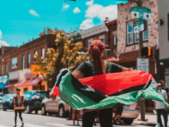 A small town street scene with a woman carrying a green, black and red flag