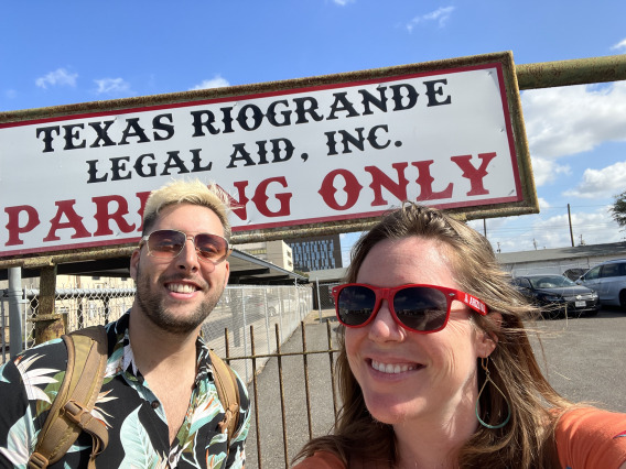 A man and woman stand smiling in front of a sign that reads Texas Rio Grande Legal Aid, Inc. Parking Only