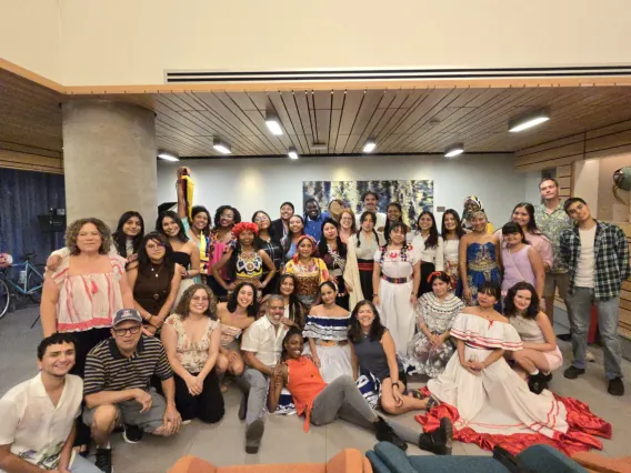 a group of students and faculty, both women and men, sit on the floor and stand, all smiling