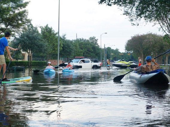 A street scene of flooding, with cars driving in deep water and a man in a canoe
