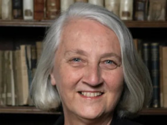 A woman with silver hair smiles in front of a bookshelf