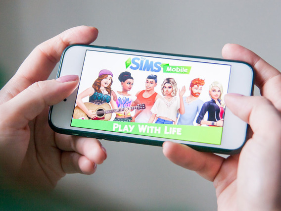 Human hands holding a phone with The Sims on the screen