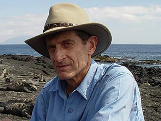 Man with blue shirt and weaing a wide-brimmed hat sits outside in a desert setting