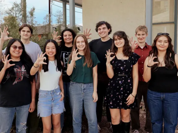 Nine students stand outside making the "Wildcat" sign with their hands