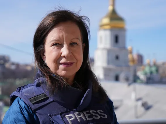 A woman wearing a blue press vest stands in front of an orthodox church