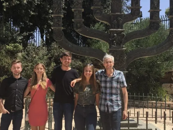 Professor and four students stand in front of a large Menorah, outside the Knesset in Jerusalem