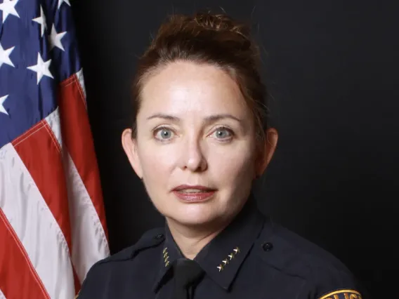 Woman in a police chief uniform (dark blue) sits in front of an American flag