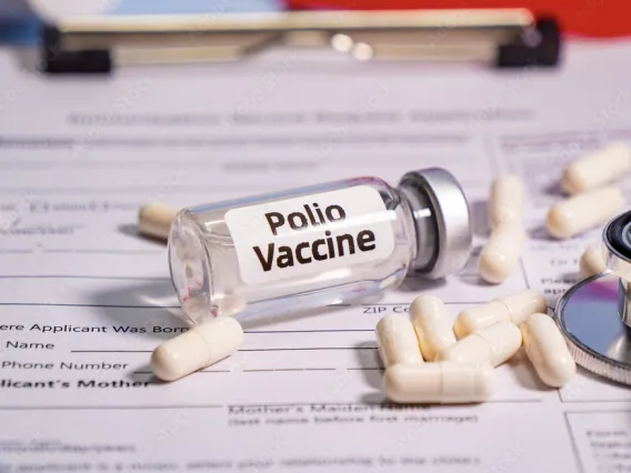 Photo of polio vaccine ampule, laying on top of paperwork, surrounded by pills and a stethoscope