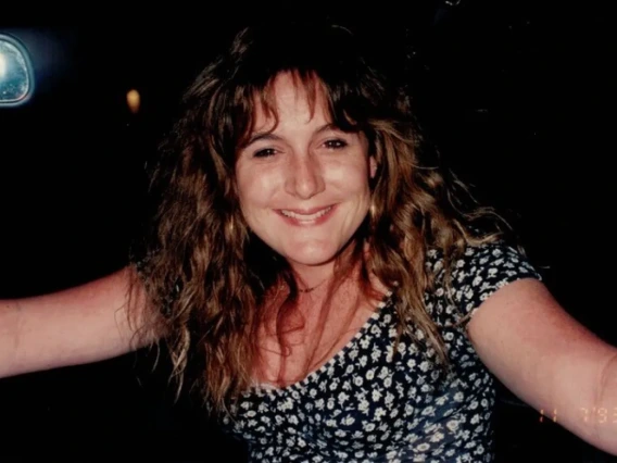 Woman with long curly hair and wearing a black and white flowered top smiles broadly