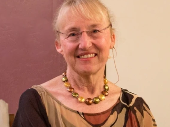Mary Stiner sits in front of a brown and white wall, smiling