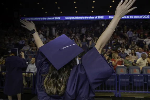 A student in graduation cap and gown waving their hands in front of a crowd.