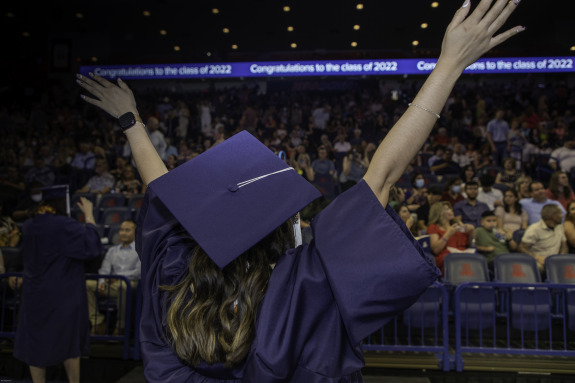 A student in graduation cap and gown waving their hands in front of a crowd.