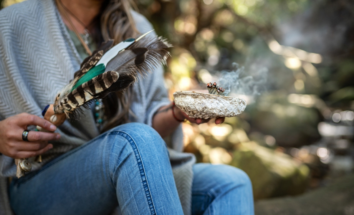 woman in jeans engaging in smudging, a rite that involves burning of sacred herbs
