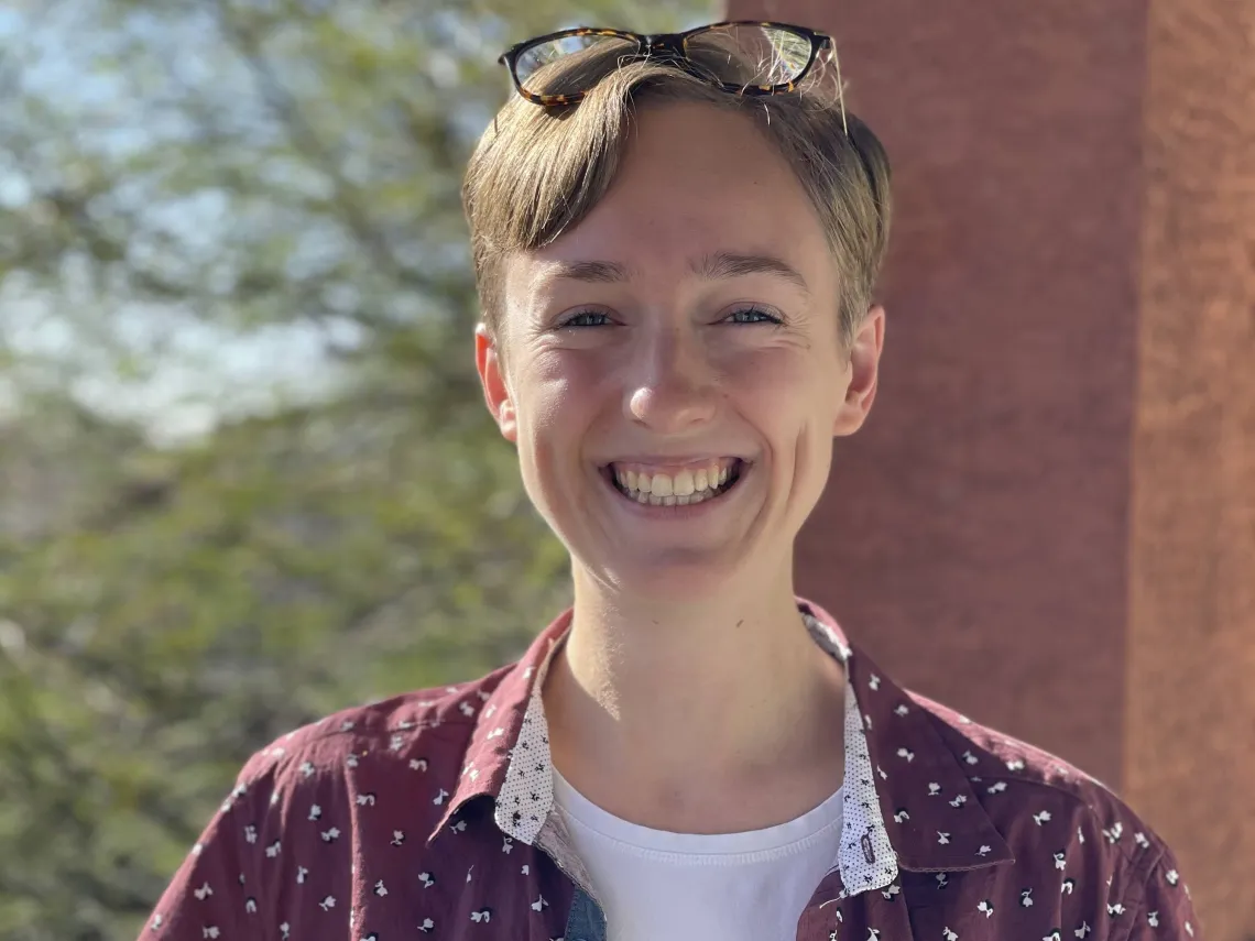 Student with short blonde hair standing outside, smiling broadly