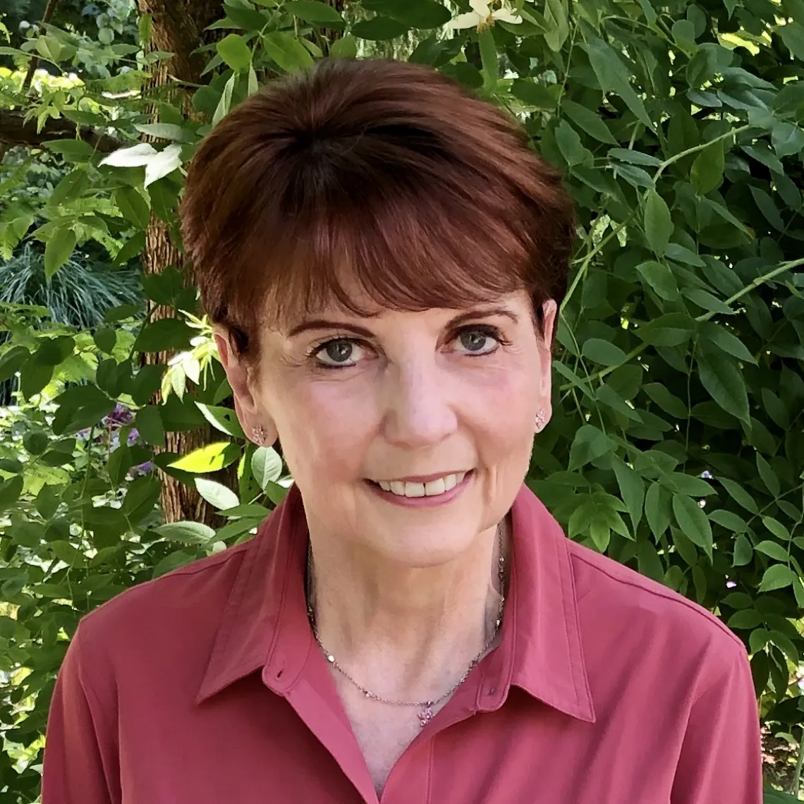 A woman with short brown hair and red shirt sits outside, smiling